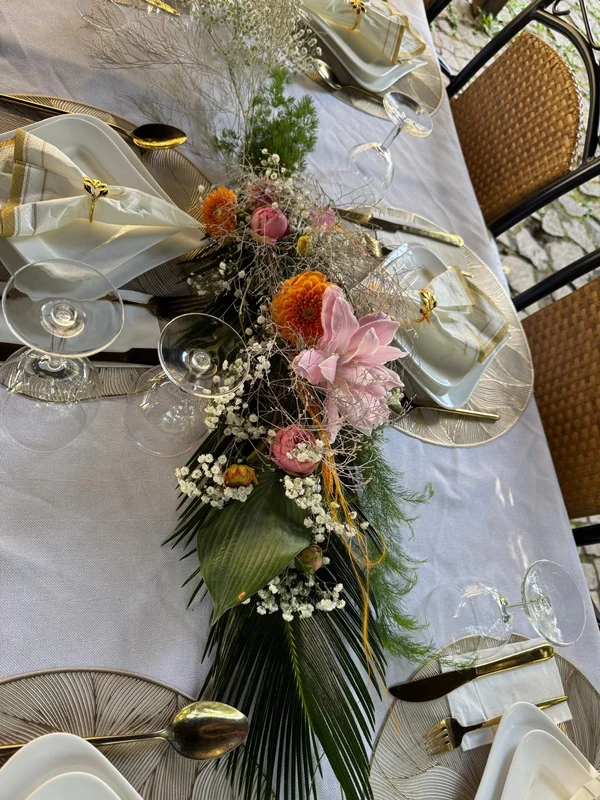 Florale Tischdekoration mit rosa und orangefarbenen Blüten und goldfarbenem Besteck